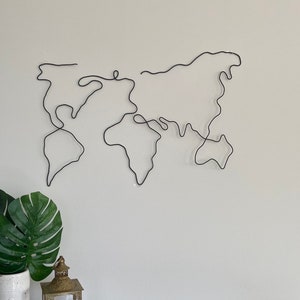 May include: A black wire sculpture of a world map on a white wall.