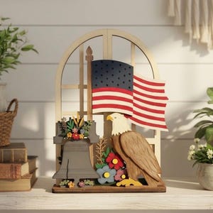 May include: Wooden patriotic decoration featuring an American flag, an eagle, and the Liberty Bell. The flag has red and white stripes with a blue field of stars. The eagle is brown and white, and the bell is gray with floral accents.