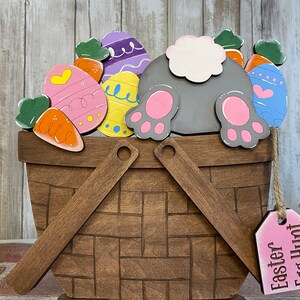 May include: A wooden Easter basket with a bunny rabbit's bottom sticking out. The basket is filled with colorful eggs and carrots. A pink tag hangs from the basket with the text "Easter Egg Hunt".