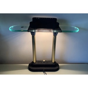 May include: A black and gold desk lamp with a glass top and a black mesh shade. The lamp has a round base and two vertical poles.