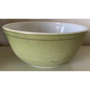 Könnte beinhalten: Eine vintage grüne Pyrex-Schüssel mit weißem Innenraum. Die Schüssel hat eine glatte, abgerundete Form und weist Gebrauchsspuren auf.