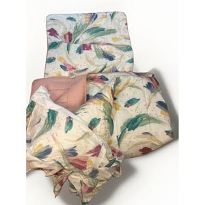 May include: A quilted bedding set featuring a white base with a painterly pattern of brushstrokes in teal, burgundy, and yellow. The set includes a comforter and matching pillow shams, with a solid dusty rose pink fabric on the reverse side.