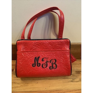 May include: Red leather handbag with a black trim and a black embroidered monogram "MFB".
