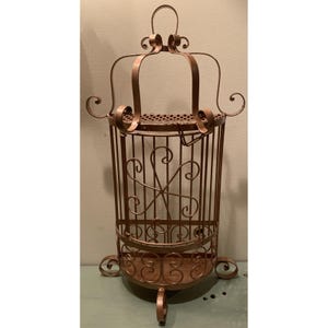 May include: A decorative, antique-style metal birdcage in a bronze finish. The cage features a crown-like top, scrolled accents, and a circular base. The cage is approximately 30 inches tall and is designed for display.