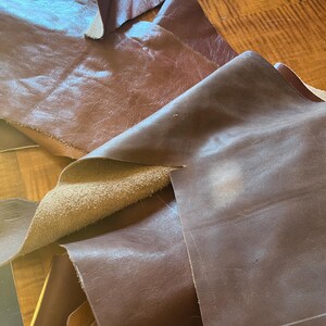 May include: A pile of brown leather scraps, some with a suede backing. The leather is smooth and appears to be of good quality.