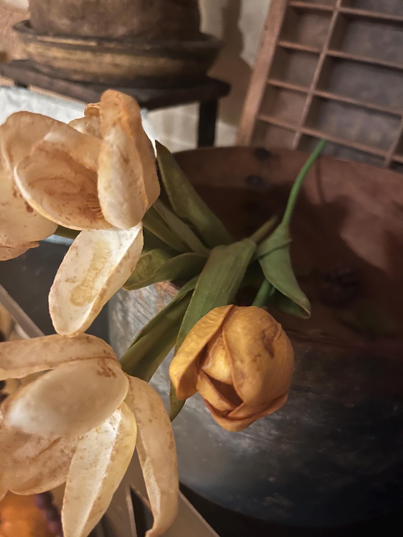 May include: A bouquet of dried flowers in shades of beige and brown, with a single yellow flower in the center, arranged in a rustic wooden bowl.