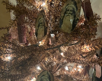 Op de afbeelding: Een rustieke kerstboom versierd met vintage kerstman ornamenten. De ornamenten zijn gemaakt van hout en hebben afbeeldingen van de kerstman met een witte baard en een rode muts. De boom is versierd met witte lampjes en heeft een bruine, takachtige uitstraling.