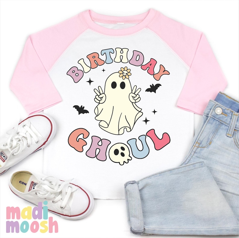 May include: A white and pink baseball tee shirt with a ghost wearing a flower on its head and the text "Birthday Ghoul" in rainbow colours.