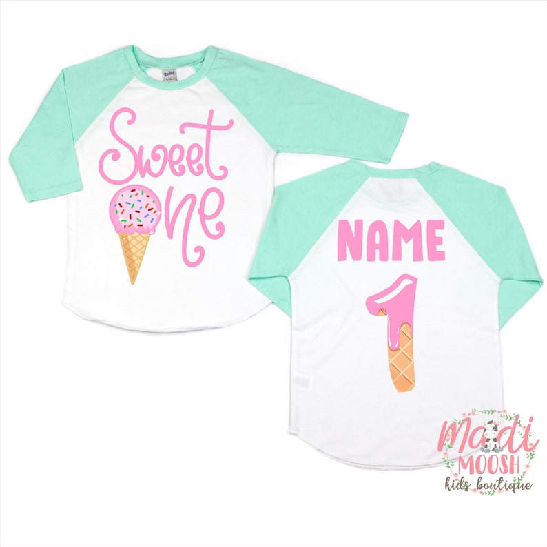 May include: A white and mint green baseball tee shirt with a pink ice cream cone graphic and the text "Sweet One" on the front. The back of the shirt has the text "NAME" and a pink ice cream cone shaped number "1".