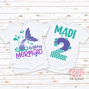 May include: White t-shirt with a purple mermaid tail and the text "Birthday Mermaid". The back of the shirt has a purple number 2 with a teal mermaid scale pattern and the name "MADI" in teal.