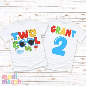 May include: Two white t-shirts with colorful graphics. One shirt says "TWO COOL" with sunglasses, a pineapple, and other summer icons. The other shirt says "GRANT 2" in bright colors. Perfect for a second birthday.