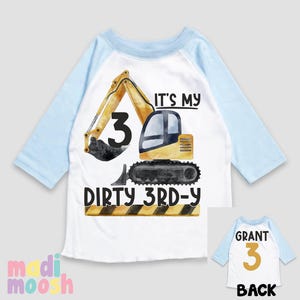 May include: A white and blue raglan t-shirt with a yellow excavator graphic and the text "It's my dirty 3rd-y". The back of the shirt has the text "Grant 3" in gold.