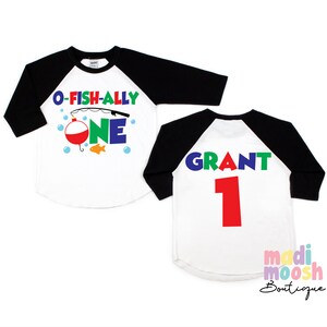 May include: White and black raglan style shirt with the text "O-FISH-ALLY ONE" and a fishing bobber and fish graphic. The back of the shirt has the name "GRANT" and the number "1" in colorful letters.