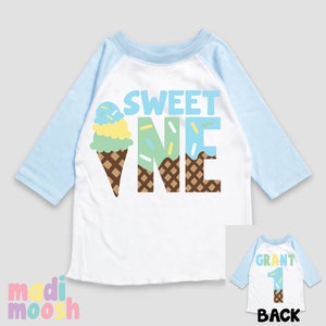 May include: White and light blue baseball style shirt with the text "SWEET ONE" and an ice cream cone graphic. The back of the shirt is light blue with the text "GRANT" and the number "1" with an ice cream cone graphic.