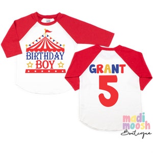 May include: Red and white baseball tee shirt with a red, white and blue circus tent graphic and the text "Birthday Boy". The back of the shirt has the name "Grant" and the number "5" in colourful letters.
