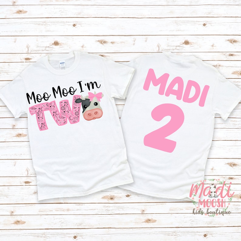 May include: Two white t-shirts with a pink cow and the text "Moo Moo I'm Two" on one shirt and the name "MADI" and the number "2" on the other shirt.