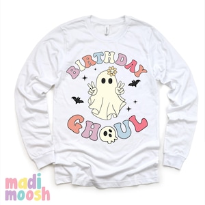 May include: White long-sleeved t-shirt featuring a colourful graphic of a ghost with a flower on its head and the text "Birthday Ghoul".