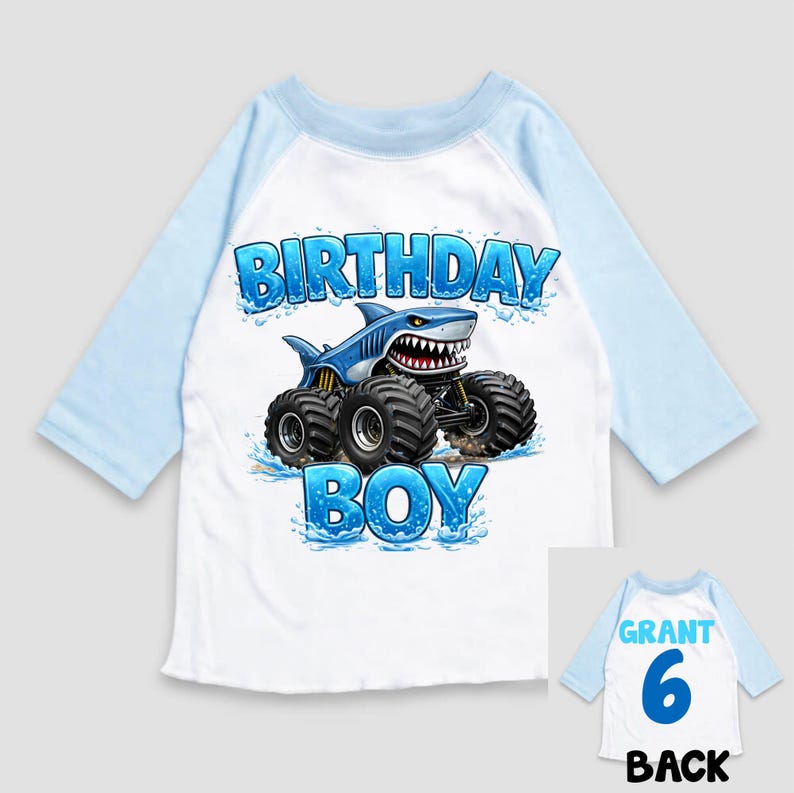 May include: A white and light blue raglan-sleeve shirt with a shark-themed monster truck graphic. The graphic includes the words "BIRTHDAY BOY". The back of the shirt has the name "GRANT", the number "6", and the word "BACK".