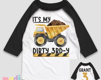 May include: White and black raglan style toddler shirt with a yellow dump truck graphic carrying brown dirt. The text "IT'S MY DIRTY 3RD-Y" is printed below the truck. The back of the shirt has the name "GRANT" and the number "3".