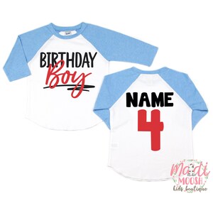 K&ouml;nnte beinhalten: Ein wei&szlig;es und blaues Baseball-Shirt mit dem Text "Birthday Boy" in Schwarz und Rot auf der Vorderseite und "NAME 4" in Schwarz und Rot auf der R&uuml;ckseite.