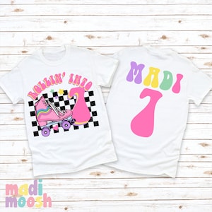 May include: White t-shirt with a pink roller skate and the text "Rollin' into 7" in a retro font. The back of the shirt has the name "MADI" in a retro font and the number "7" in pink.