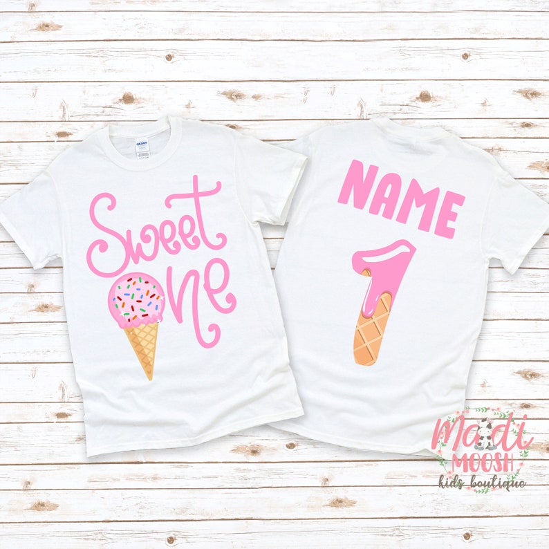 May include: White t-shirt with pink text that says "Sweet One" and a pink ice cream cone with sprinkles. The back of the shirt has a pink number "1" shaped like an ice cream cone with the text "NAME" above it.