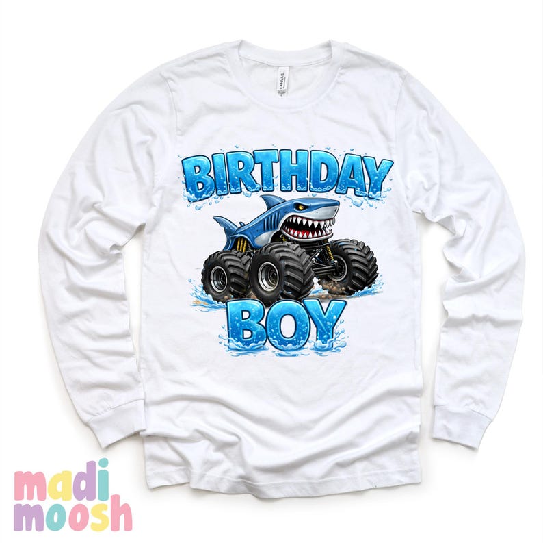 May include: White long-sleeve shirt with a graphic of a blue shark monster truck. The text "BIRTHDAY BOY" is in blue, with water splash accents. The shirt has a crew neck and long sleeves.