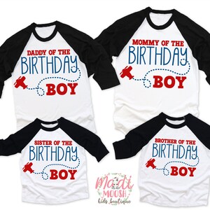 May include: Set of four white and black baseball shirts with red and blue text. The shirts say "Mommy of the Birthday Boy", "Daddy of the Birthday Boy", "Sister of the Birthday Boy", and "Brother of the Birthday Boy". Each shirt has a small red airplane graphic with a blue dotted line.
