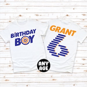 May include: Two white t-shirts with a birthday theme. The front shirt has the text "Birthday Boy" in blue with a target graphic in orange and blue. The back shirt has the name "GRANT" in orange and a number "6" made of blue and orange bullets.