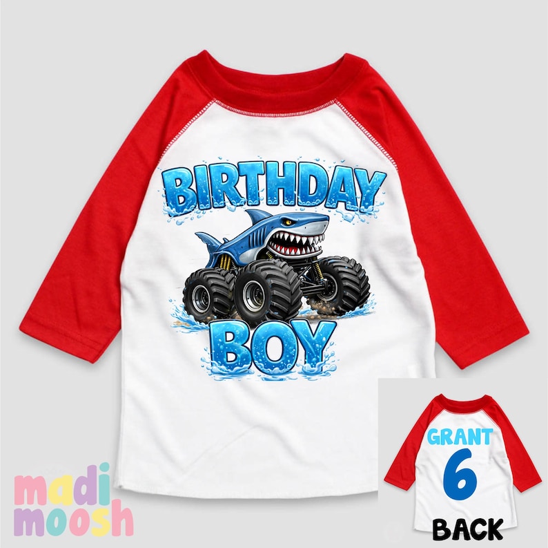 May include: White and red raglan-style birthday shirt with a shark-themed monster truck graphic. The front of the shirt says "BIRTHDAY BOY" in blue, while the back has "GRANT 6" printed on it.