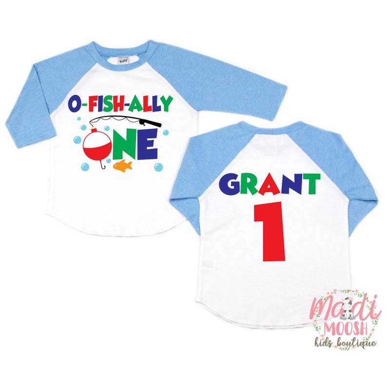 May include: White and light blue raglan style shirt with the text "O-FISH-ALLY ONE" and a fishing theme graphic on the front. The back of the shirt has the name "GRANT" and the number "1" in red.