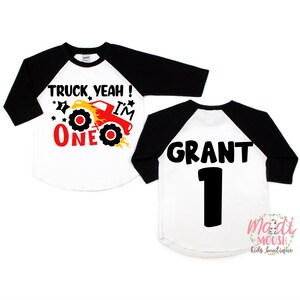 May include: A white and black baseball style shirt with a red monster truck graphic and the text "Truck Yeah! I'm One" on the front. The back of the shirt has the name "Grant" and the number "1" in black.