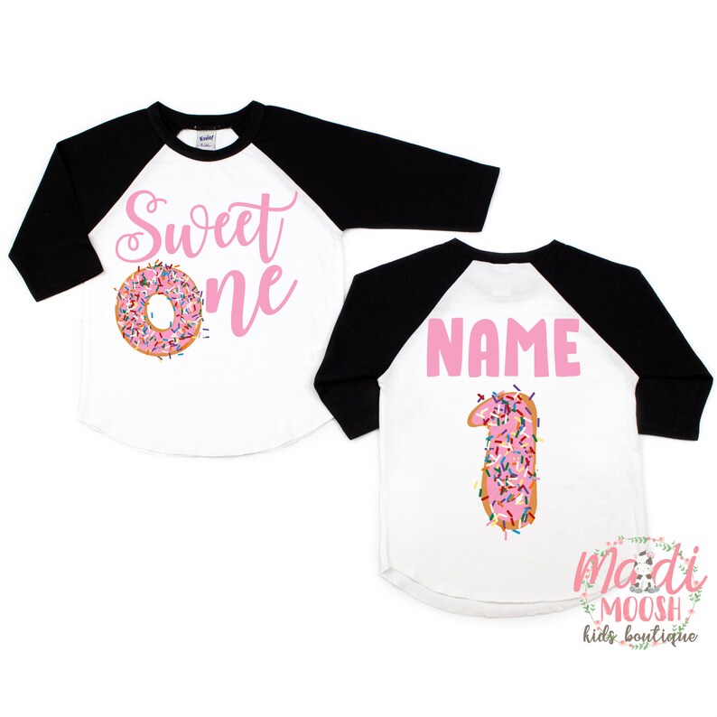 May include: Two white and black baseball shirts with pink text. One shirt says "Sweet One" with a pink donut with sprinkles. The other shirt says "NAME" with a pink donut shaped like the number one with sprinkles.