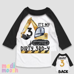 May include: A white and black baseball tee shirt with a yellow excavator design. The shirt says "It's my dirty 3rd-y" and has a yellow number 3 on the excavator. The back of the shirt has a yellow number 3 and the word "Grant" on it.
