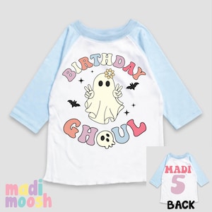May include: A white and blue baseball tee shirt with a rainbow coloured graphic of a ghost with the text "Birthday Ghoul". The back of the shirt has the text "Madi 5" in pink.