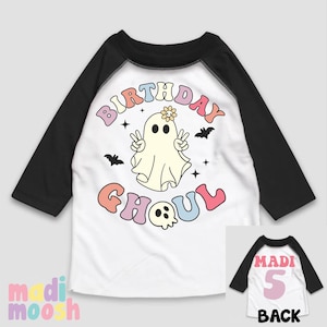 May include: White and black baseball tee shirt with a rainbow coloured "Birthday Ghoul" graphic featuring a ghost with a flower on its head. The back of the shirt has a pink number 5 and the word "Madi" in black.
