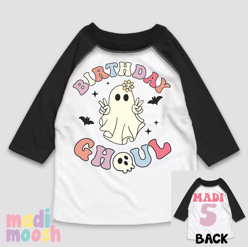 May include: White and black baseball tee shirt with a rainbow coloured "Birthday Ghoul" graphic featuring a ghost with a flower on its head. The back of the shirt has a pink number 5 and the word "Madi" in black.