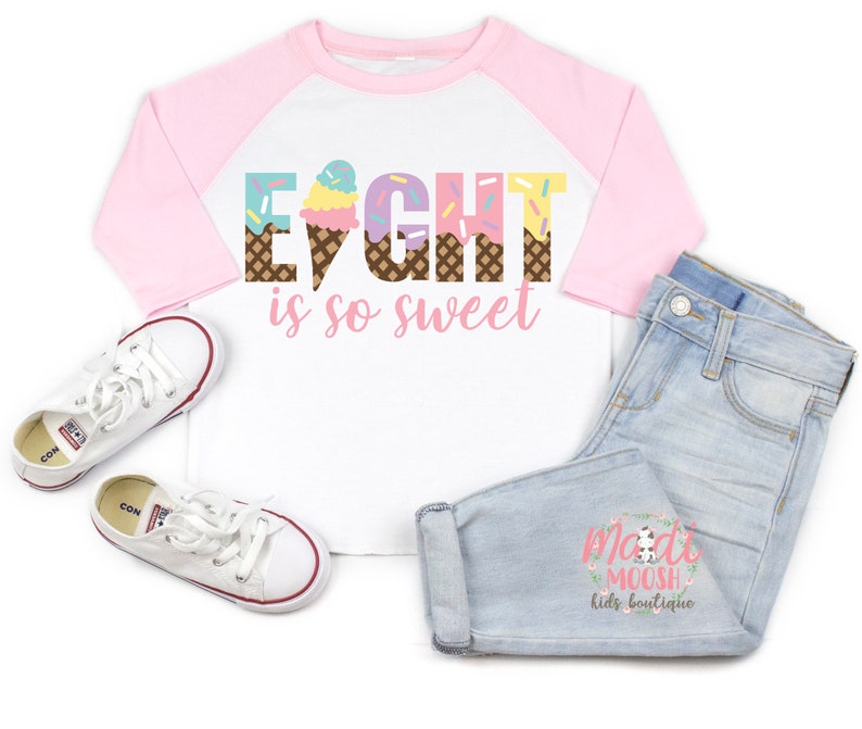 May include: A white and pink baseball tee shirt with the words "Eight is so sweet" in rainbow colors with ice cream cone graphics. The shirt has a pink and blue color block design.