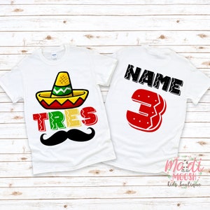 May include: White t-shirt with a colorful sombrero, the word "TRES" in green, yellow, and red, and a black mustache. The back of the shirt has the word "NAME" and the number "3" in red.