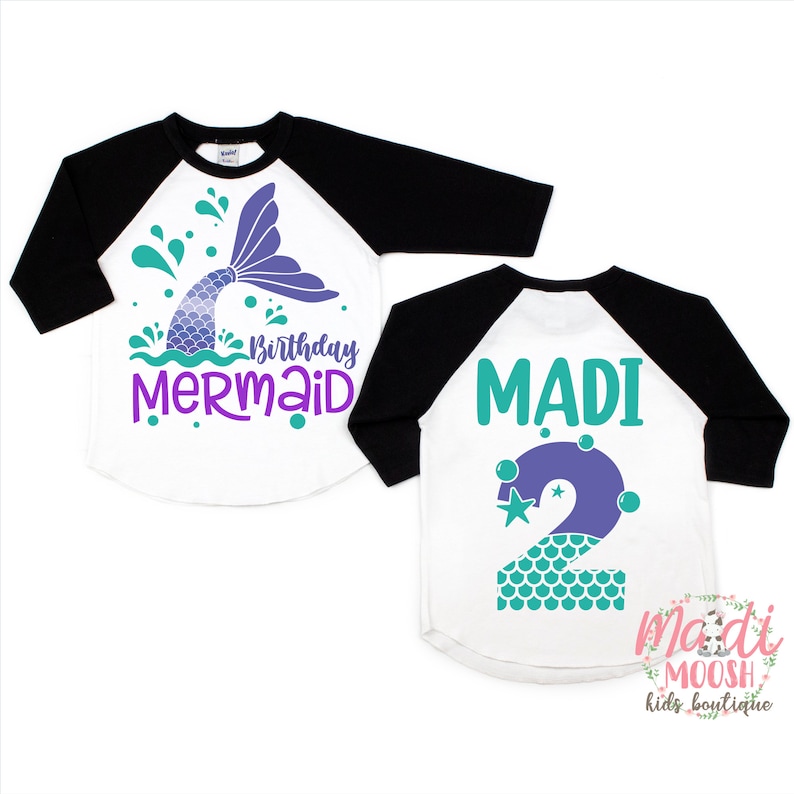 May include: Two white and black baseball shirts with a mermaid theme. One shirt has a purple mermaid tail with green water and the text "Birthday Mermaid". The other shirt has a purple number "2" with green scales and stars. Both shirts have the text "Madi" on them.