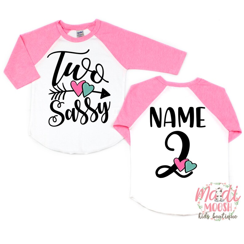May include: A white and pink raglan style toddler shirt. The front of the shirt says "Two Sassy" with an arrow and hearts. The back of the shirt says "Name" and the number "2".