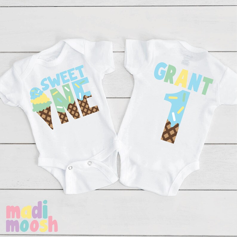 May include: Two white baby onesies with an ice cream cone theme. One onesie says "Sweet One" with a blue and green ice cream cone and sprinkles. The other onesie says "Grant 1" with a blue ice cream cone and sprinkles.