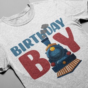 May include: A gray t-shirt with the text "Birthday Boy" in blue and red letters. A cartoon train engine is behind the "B" in the word "Boy".
