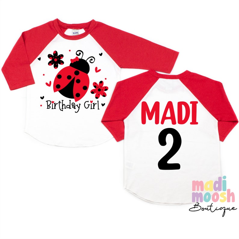 May include: Red and white baseball style shirt with a ladybug and flowers on the front and the name "MADI" and the number "2" on the back.