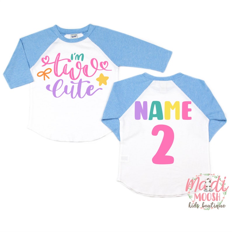 May include: A white and blue baseball style shirt with the text "I'm two cute" in colorful letters on the front and the text "NAME 2" on the back.