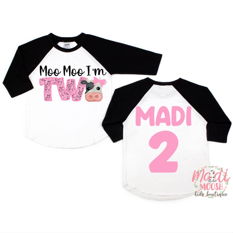 May include: A white and black baseball style shirt with pink lettering that says "Moo Moo I'm Two" with a cow graphic. The back of the shirt says "MADI 2" in pink lettering.