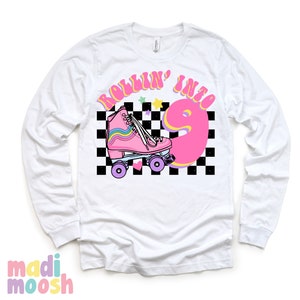 May include: White long-sleeve shirt with a pink roller skate and the text "Rollin' into 9" in a retro font. The background is a black and white checkered pattern with stars.
