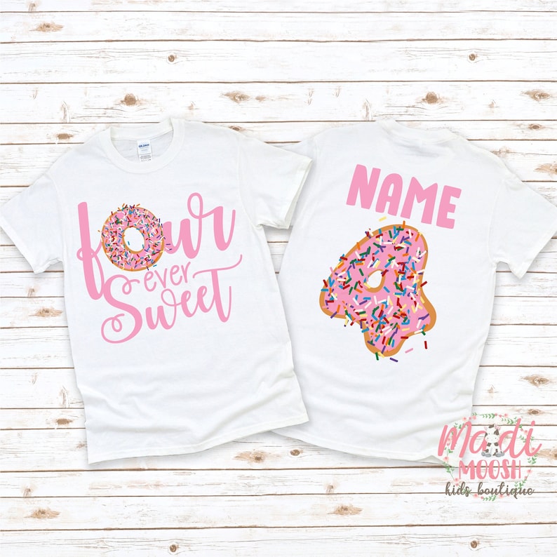 以下が含まれることがあります： 半袖の白いTシャツ2枚。左のTシャツにはピンク色の文字で「four ever Sweet」と書かれており、「o」の代わりにドーナツが描かれています。右のTシャツにはピンク色の文字で「NAME」と書かれ、その下にカラフルなスプリンクルがトッピングされたドーナツ型の大きな数字の「4」がデザインされています。