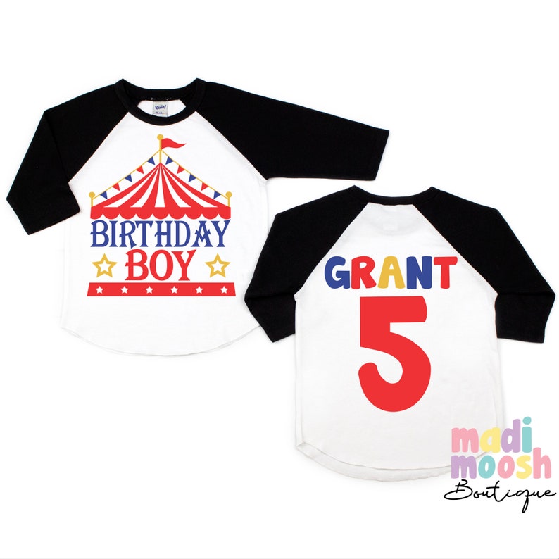 May include: A white and black baseball style shirt with a red, white and blue circus tent graphic and the text "Birthday Boy" on the front. The back of the shirt has the name "GRANT" in colourful letters and the number "5" in red.