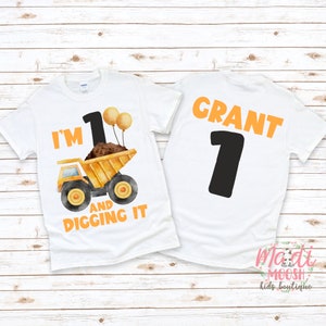 May include: A white t-shirt with a yellow dump truck and the text "I'm 1 and digging it". The back of the shirt has the name "Grant" and the number "1" in black.